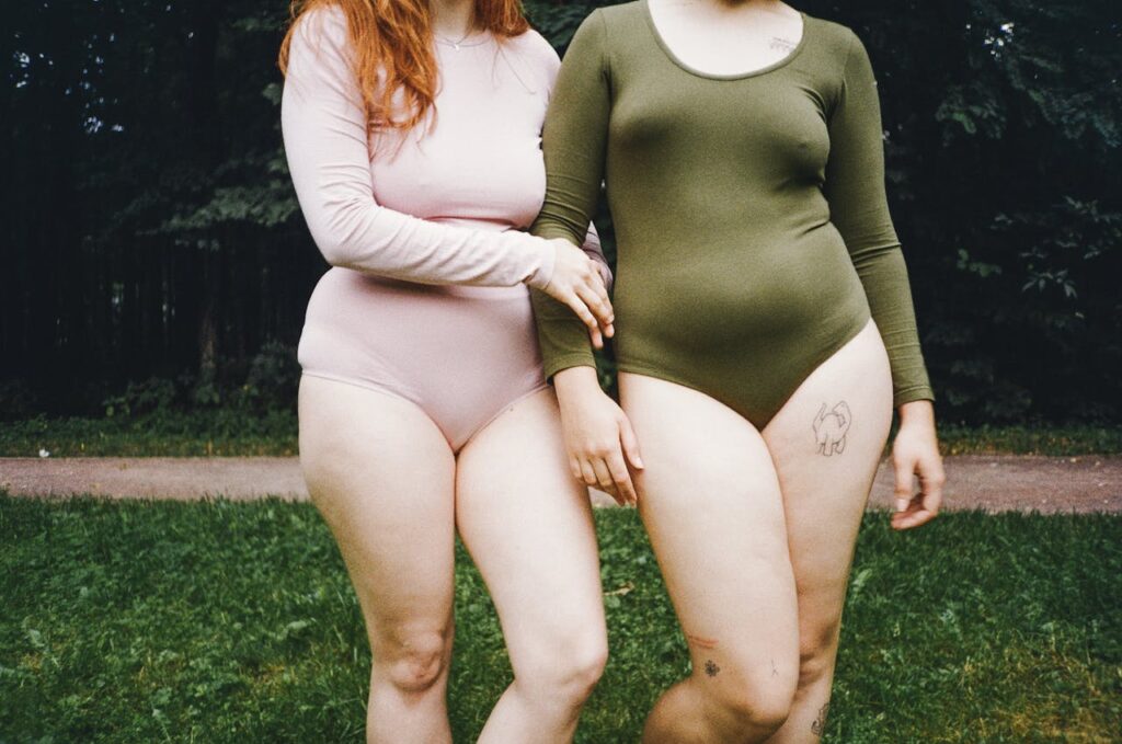 Two women in bodysuits celebrating body positivity in a natural setting.